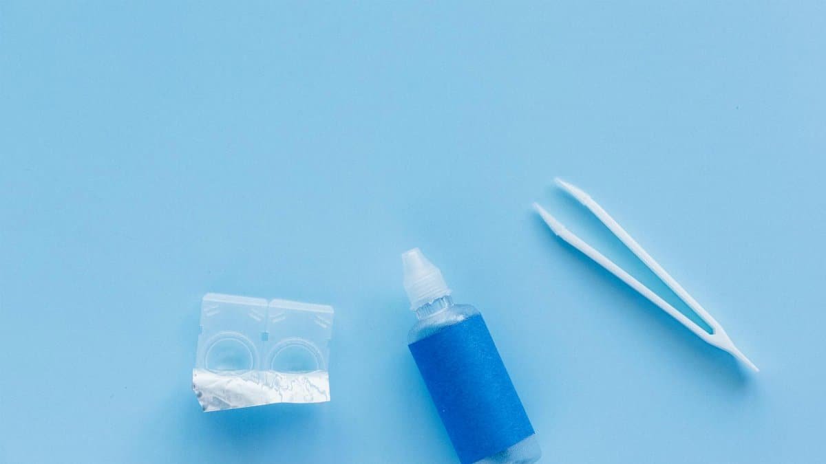 Flat lay of contact lenses, solution bottle, and tweezers on a blue background.