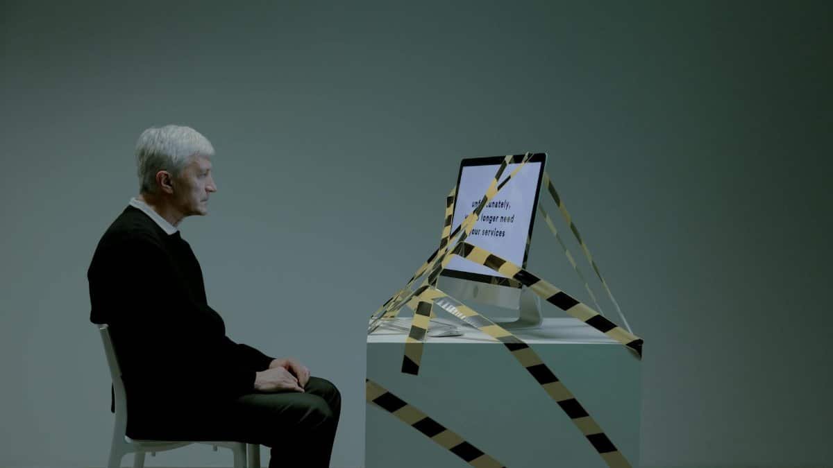An elderly man sits contemplating job loss, surrounded by caution tape, symbolizing unemployment and ageism.