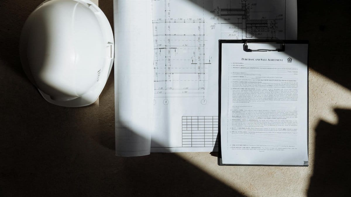 Top view of construction documents and hard hat in sunlight, capturing planning essence.