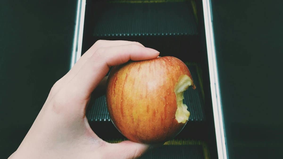 Hand holding a bitten apple on an escalator, showcasing a blend of food and travel concept.
