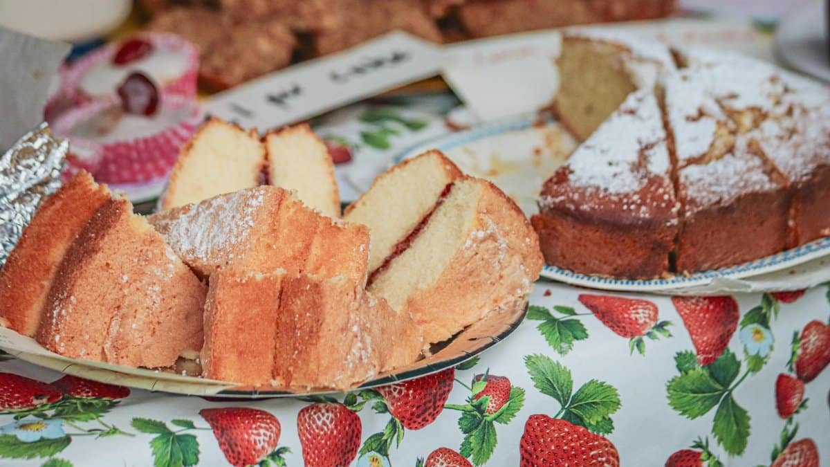 Close-up view of sliced sponge and pound cakes on a strawberry-patterned tablecloth.