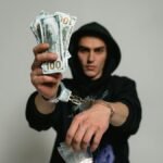 Close-up of a man in handcuffs holding cash and drugs, illustrating crime and illegal activities.