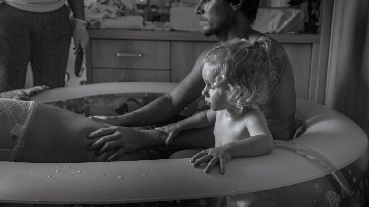 Black and white photograph capturing a supportive family during a home water birth.