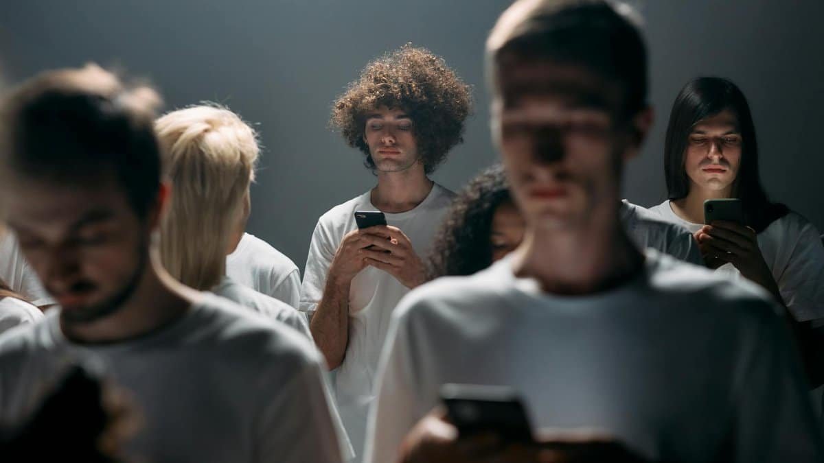Group of young adults absorbed in smartphones under dramatic lighting, illustrating social isolation.