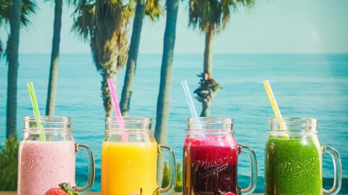 Vibrant smoothies in mason jars with a tropical ocean backdrop, perfect for refreshment.