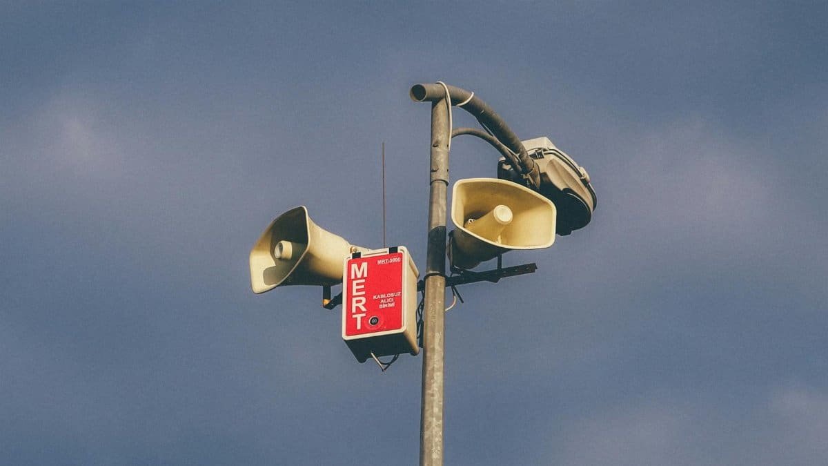 A warning system with loudspeakers on a pole against a cloudy sky, signaling emergency alerts.