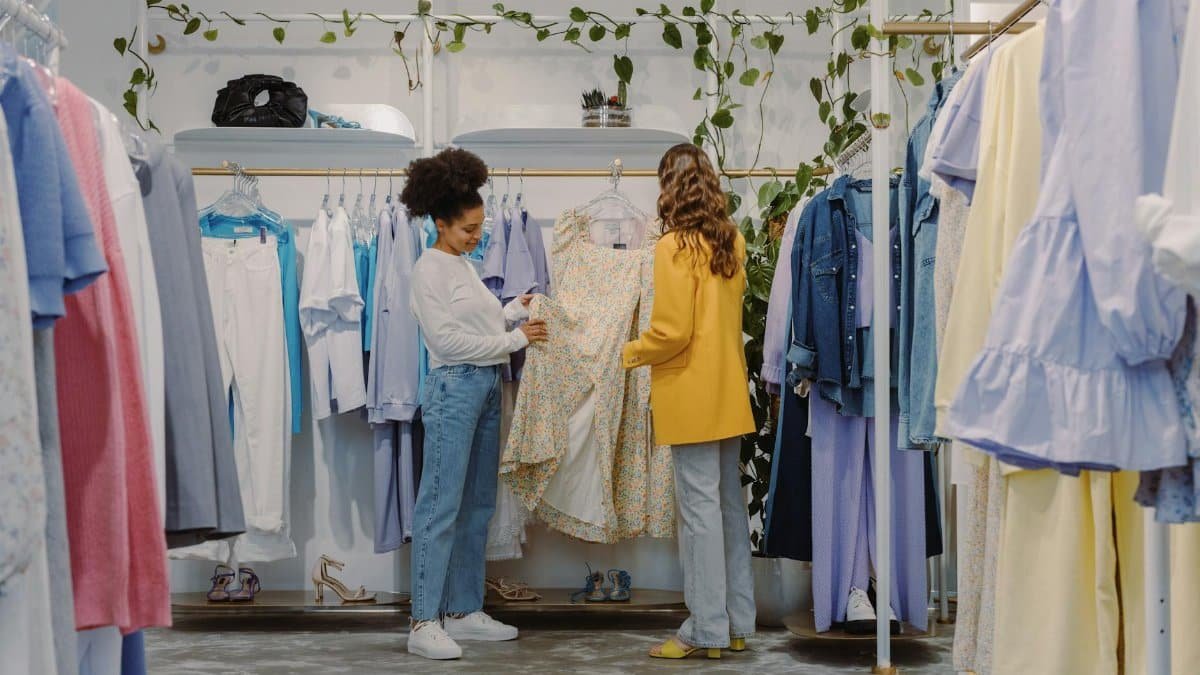 Two women shopping for trendy outfits in a modern clothing boutique filled with colorful garments.