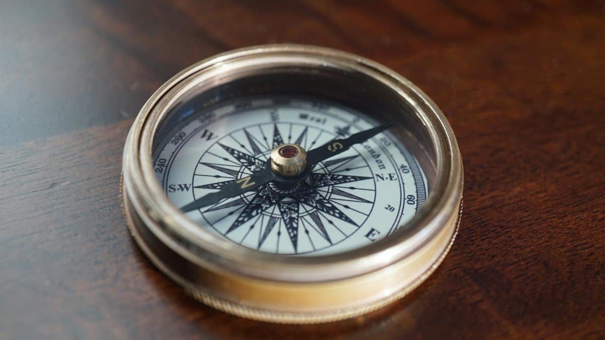 Close-up of a vintage compass resting on a warm, dark wooden surface, indicating navigation and exploration.