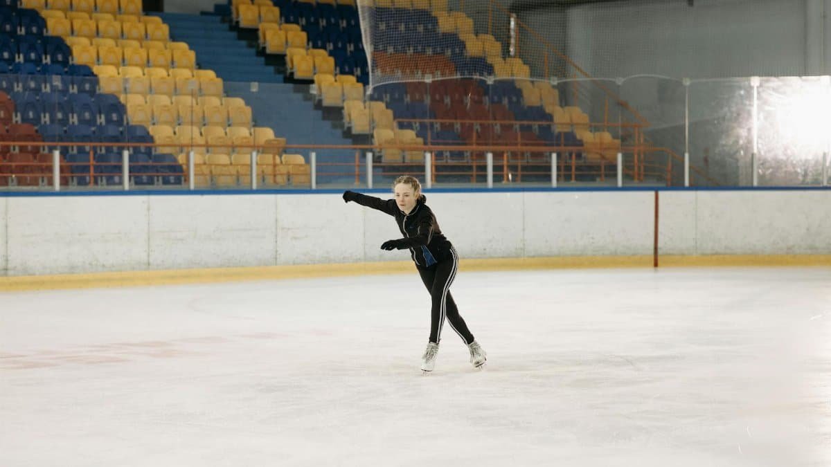 A young woman elegantly figure skating on an indoor ice rink, showcasing her skills.