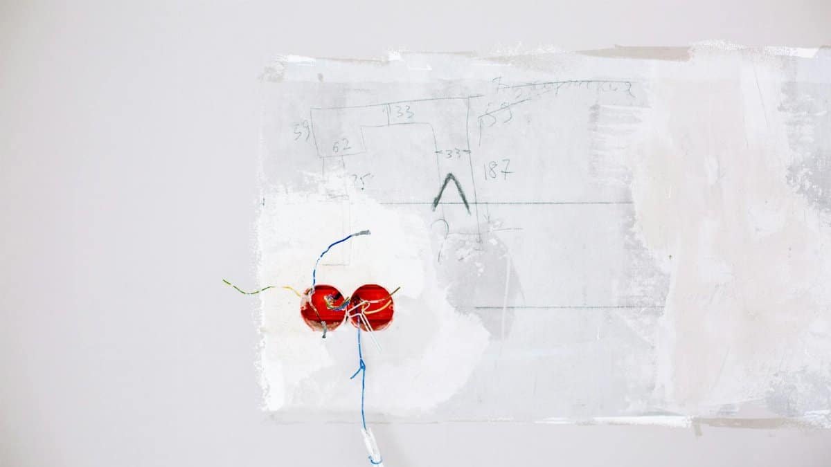 Close-up view of exposed electric wiring being installed during home renovation on a white wall.