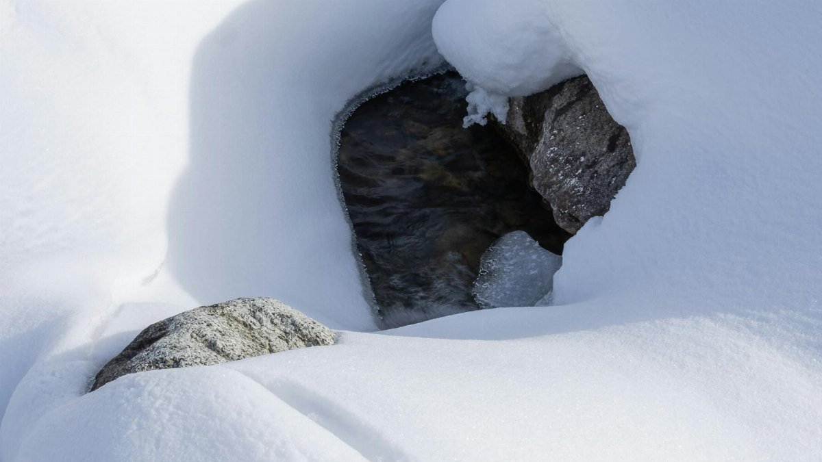 A tranquil winter scene featuring a snow-covered stream amidst rocky terrain.
