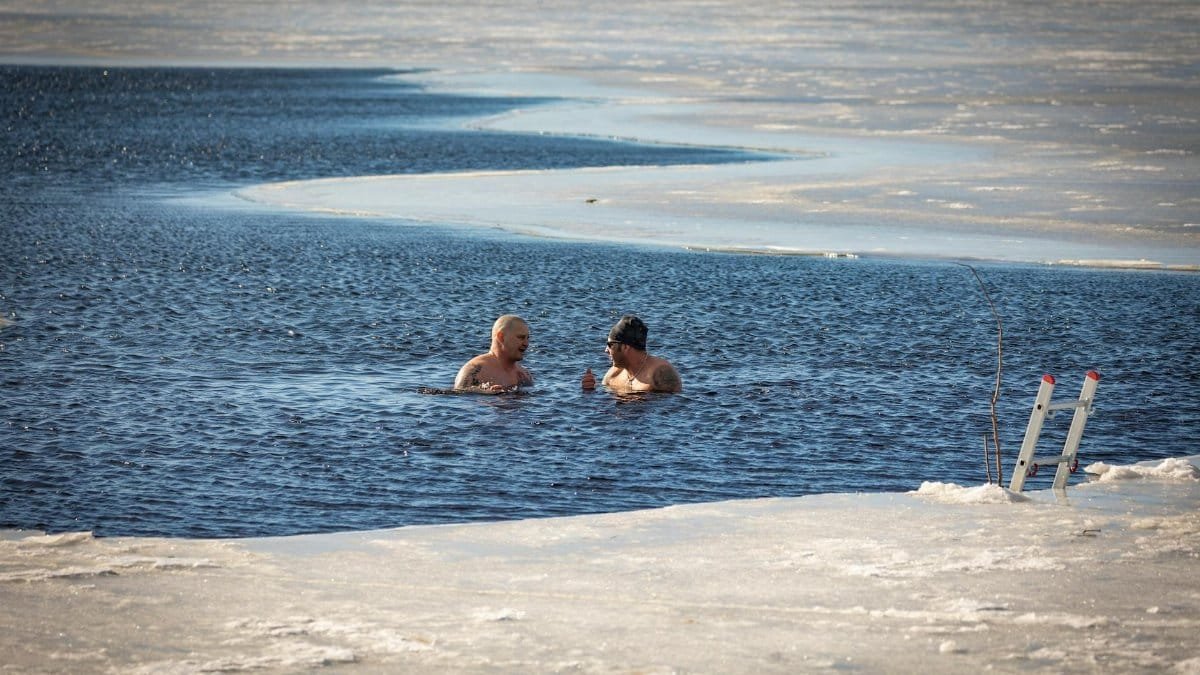 Two men brave the cold for a swim in a partially frozen lake during winter.