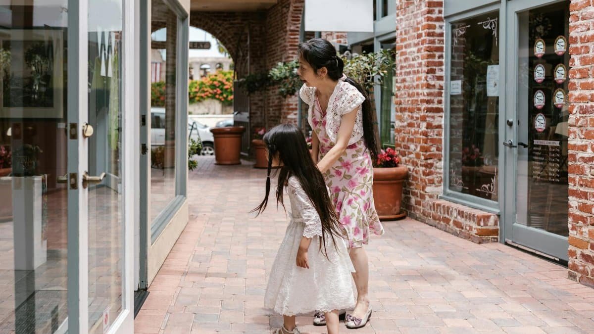 A mother and daughter window shopping in a charming urban brick-lined walkway.