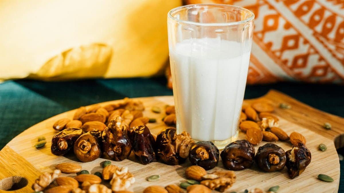 A refreshing glass of milk surrounded by dates, almonds, and nuts on a wooden board.