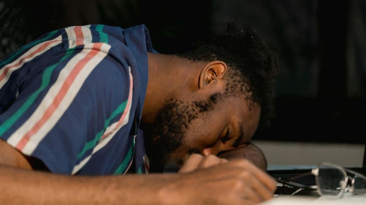 A man with facial hair rests his head on a desk, napping during a late work session.