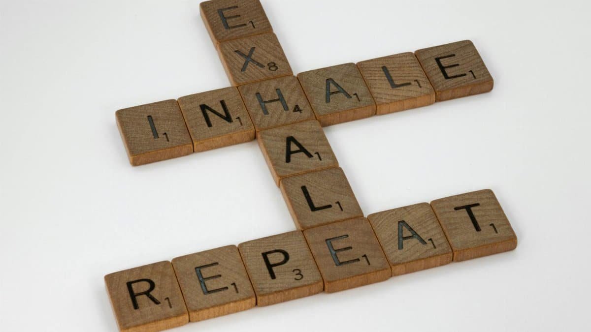 Wooden Scrabble tiles arranged to form the words 'Inhale, Exhale, Repeat' on a white background.
