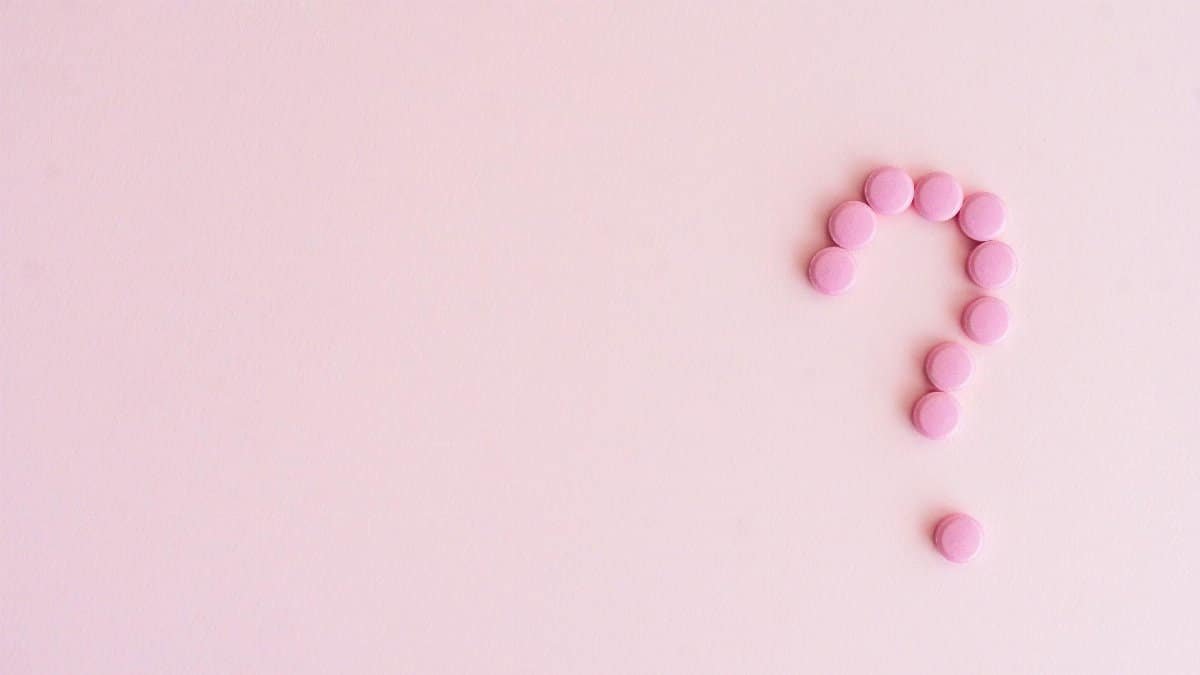 A question mark created from pink pills on a light pink surface, symbolizing uncertainty in health decisions.