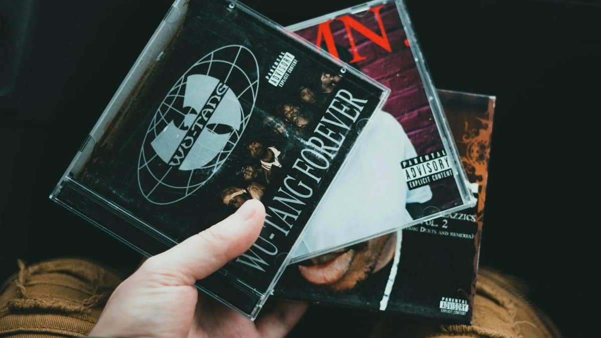 A hand holding a collection of classic hip hop CDs showcasing iconic album covers.