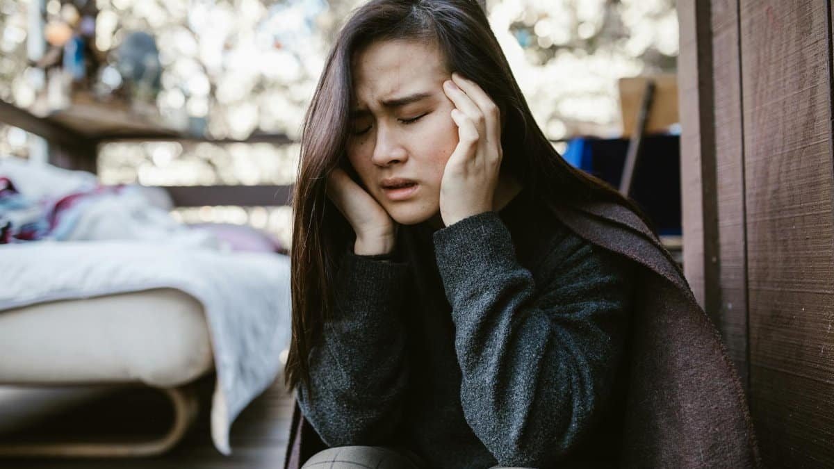 A young woman holds her head in distress while sitting indoors, capturing an emotional moment.
