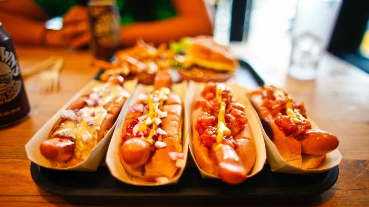 Close-up of various hotdogs with toppings on a wooden table, ideal for fast food themes.