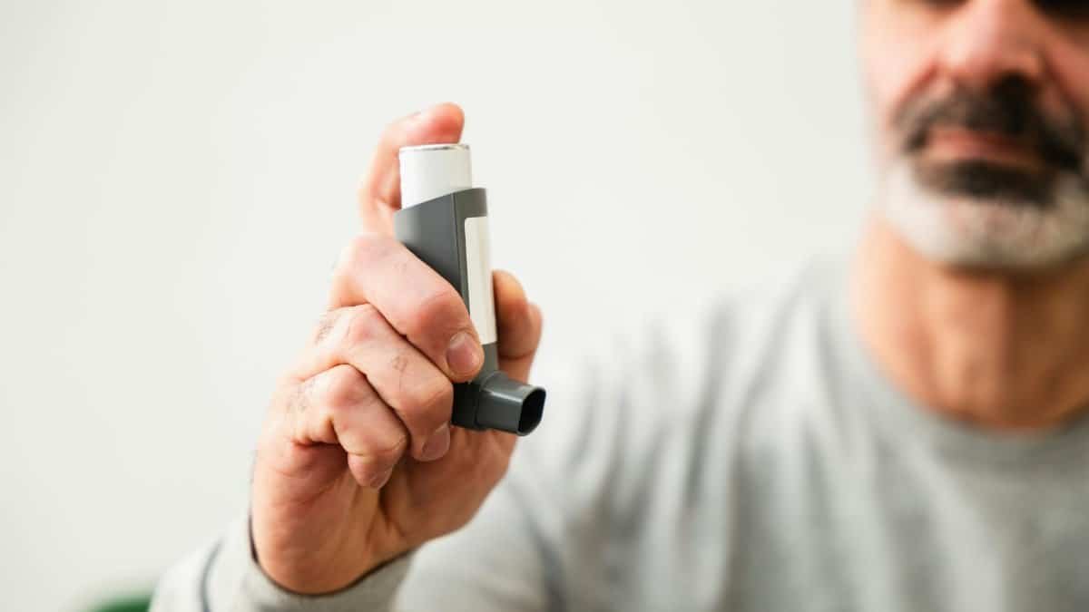 Middle-aged man using an inhaler to manage respiratory issues indoors.