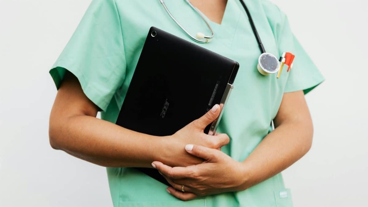 Close-up of a nurse in green scrubs holding a tablet and stethoscope, symbolizing modern healthcare.