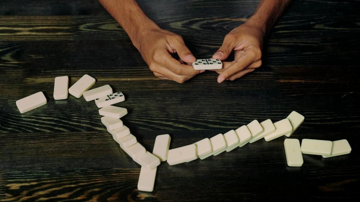 High-angle view of hands holding and arranging dominoes on a wooden table symbolizing strategy and impact.