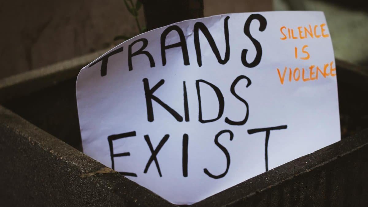 Close-up of a sign with the message 'Trans Kids Exist' advocating for transgender rights and awareness.