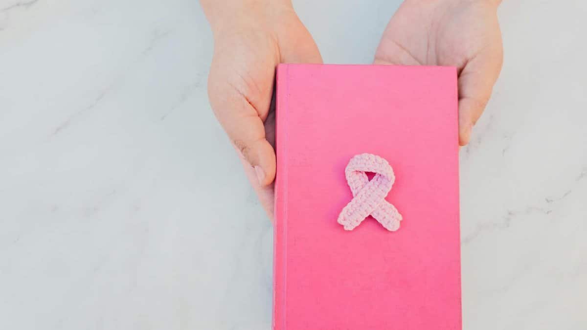 Hands holding a pink book with a breast cancer awareness ribbon, symbolizing support.