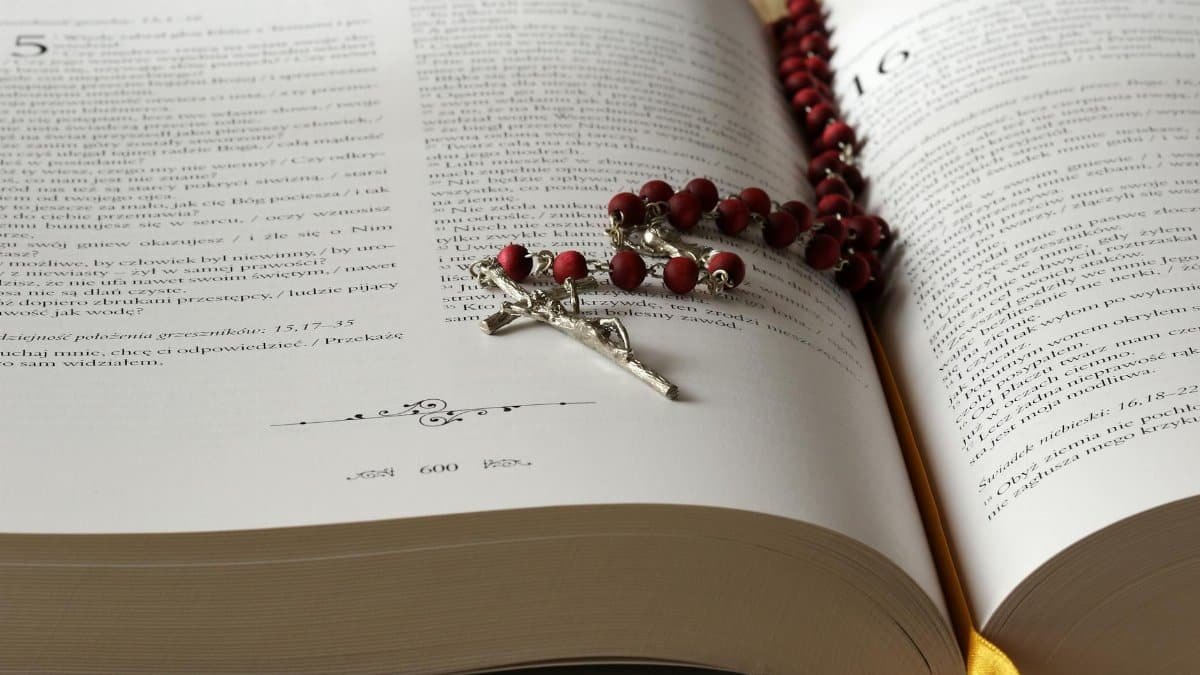 Open Bible with red rosary beads draped on pages, symbolizing faith and devotion.