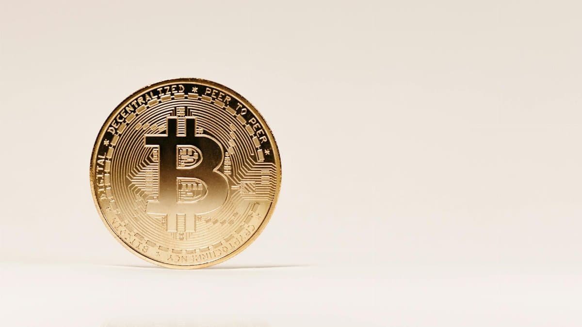 Close-up of a golden Bitcoin coin standing upright on a neutral background, showcasing cryptocurrency symbolism.