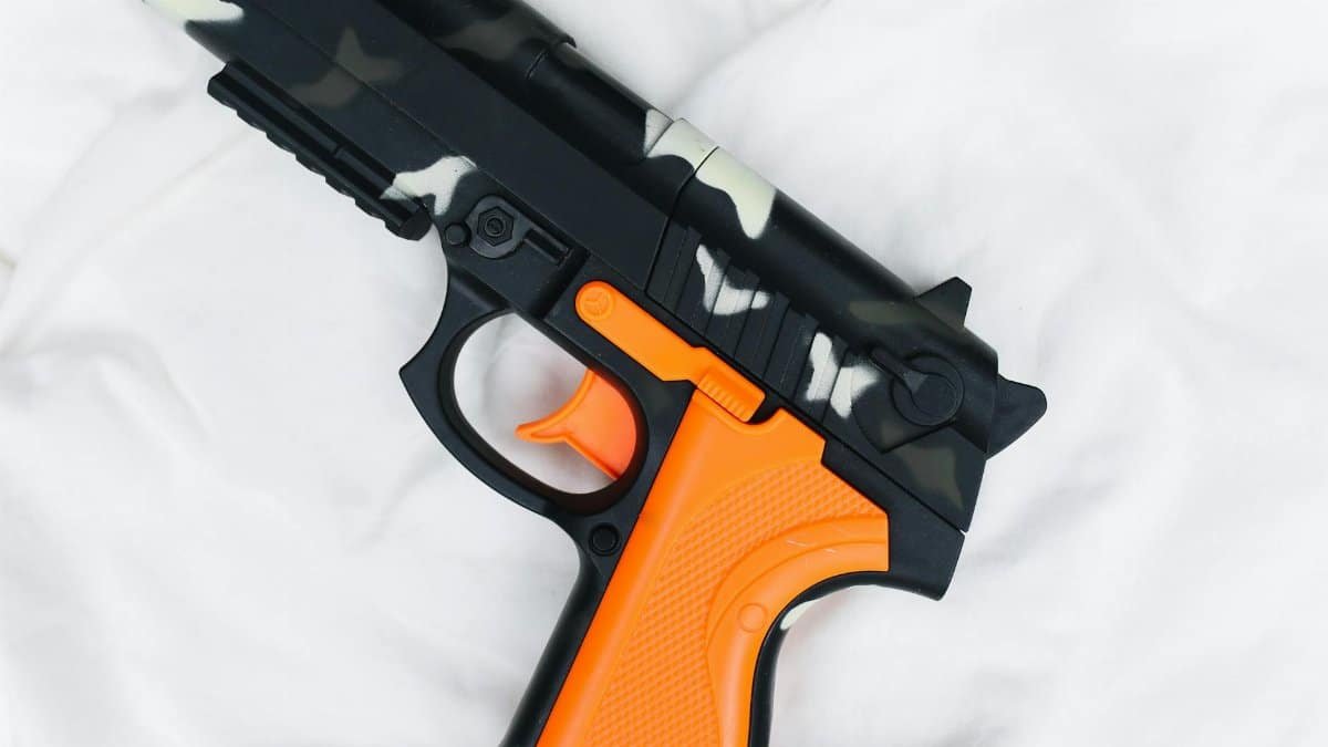 Close-up of a camouflage toy gun with orange features on a soft white fabric, creating contrast.