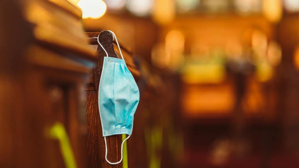 A blue facemask hangs on a wooden church pew, symbolizing safety protocols and community resilience.