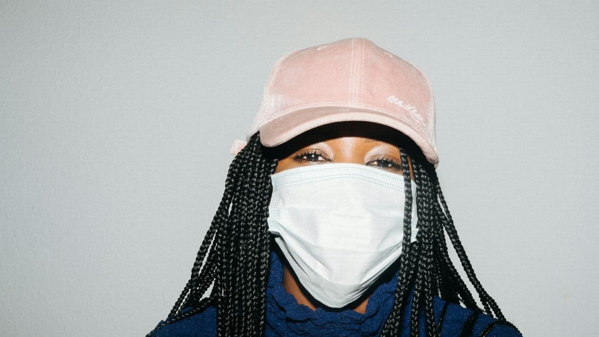 Portrait of a young woman wearing a mask and cap in a studio setting, showcasing modern health fashion.