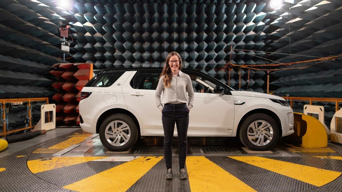 Female engineer stands in anechoic chamber with a car for sound testing.
