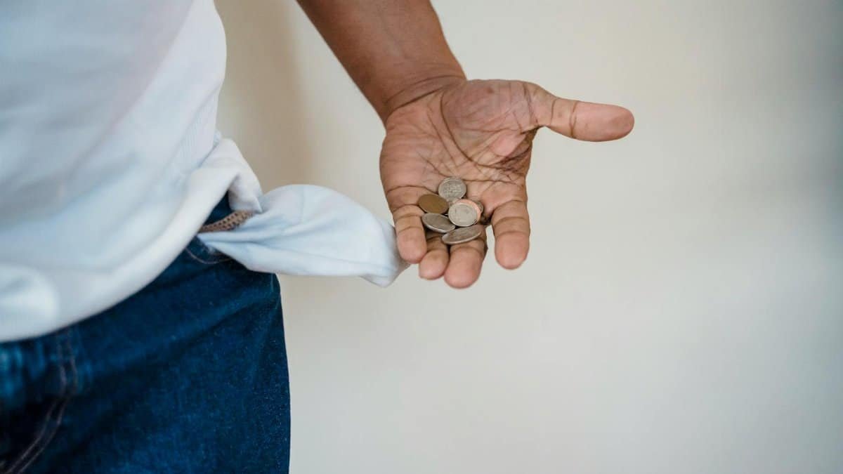 A close-up of a person holding coins with a turned-out empty pocket, illustrating financial struggle.