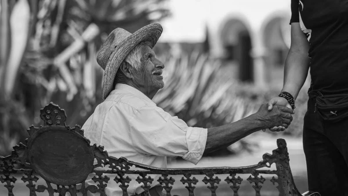 Elderly man in traditional attire shakes hands in a Cholula street. Black and white portrait.