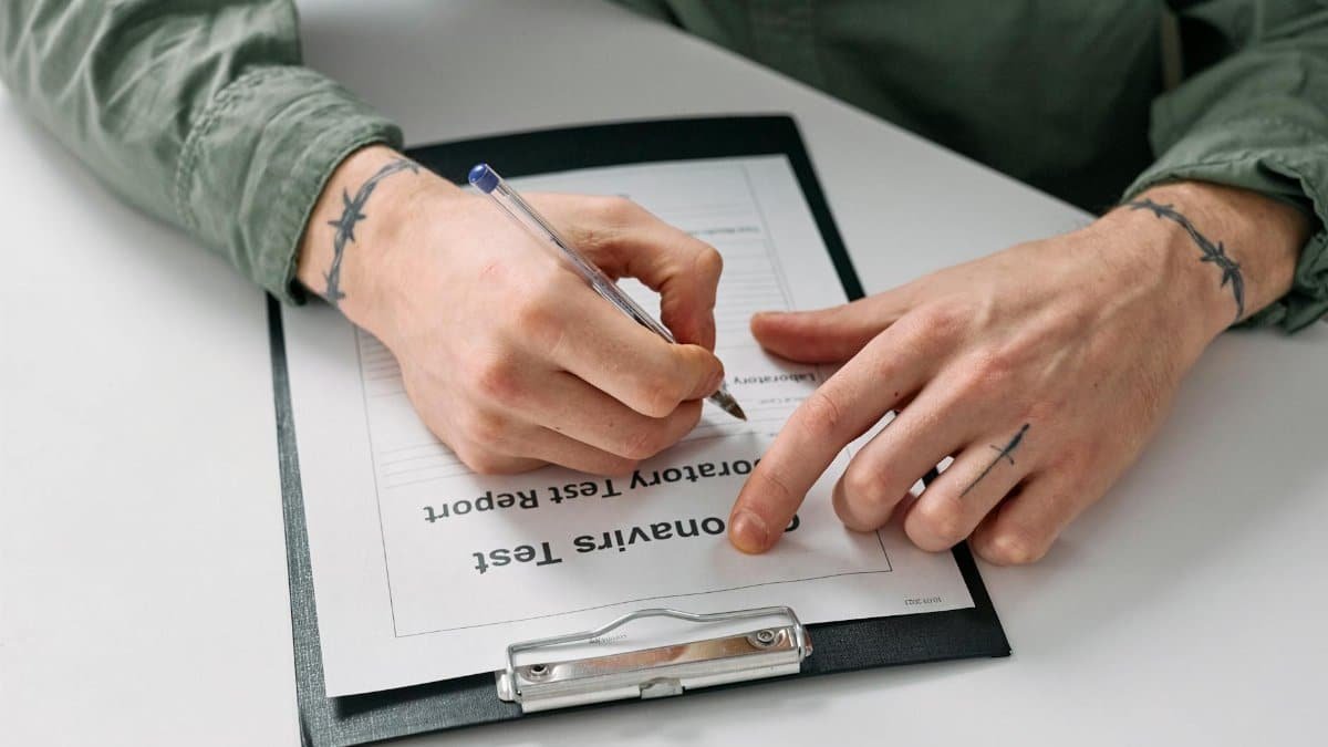 A person with tattoos writes on an honesty test report using a pen and notepad.