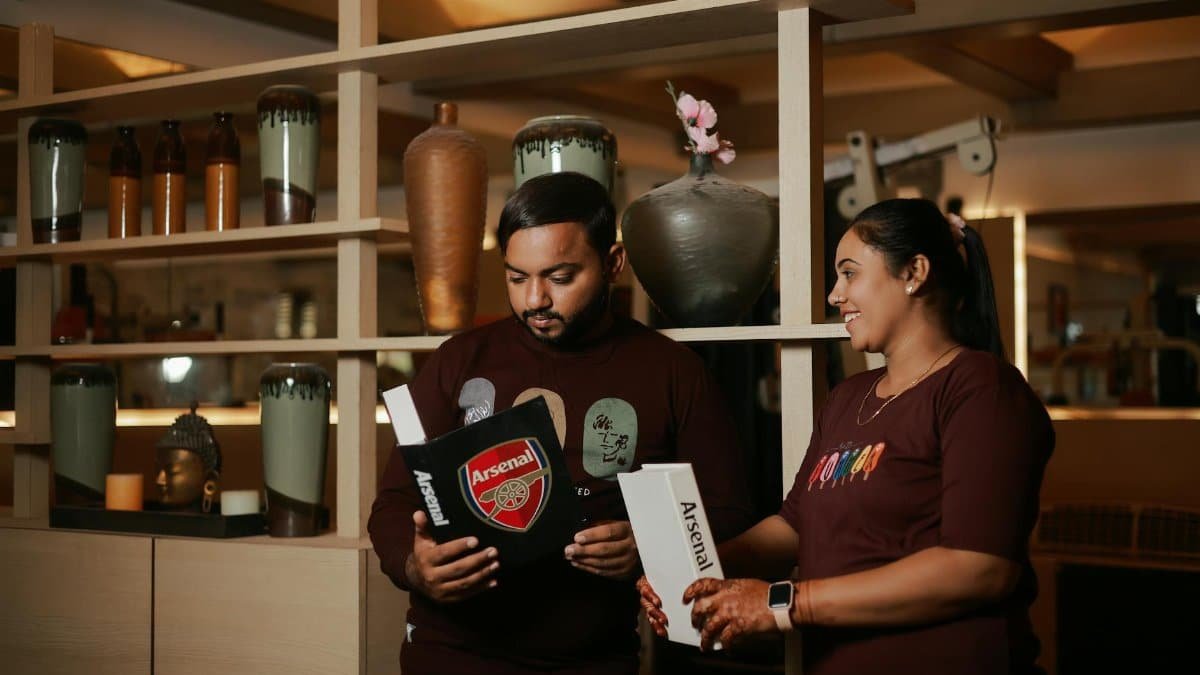 Couple exchanging Arsenal-themed gifts in warm, cozy cafe setting.