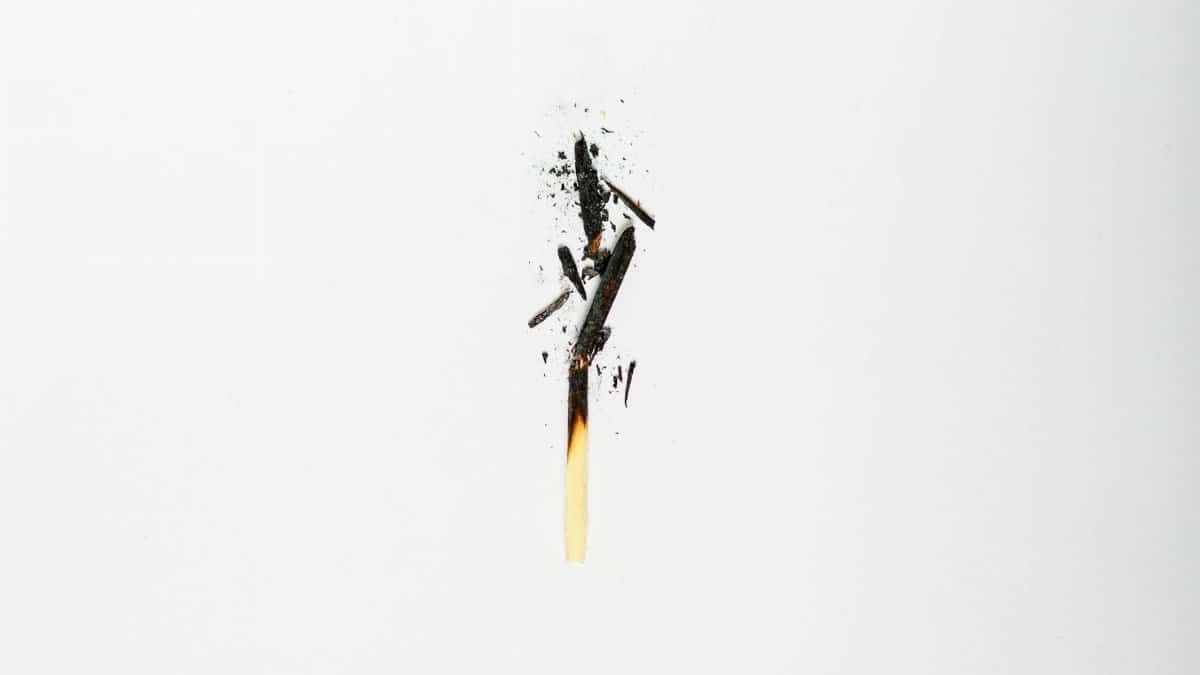 Minimalist image of a burnt matchstick with scattered ash on white background.