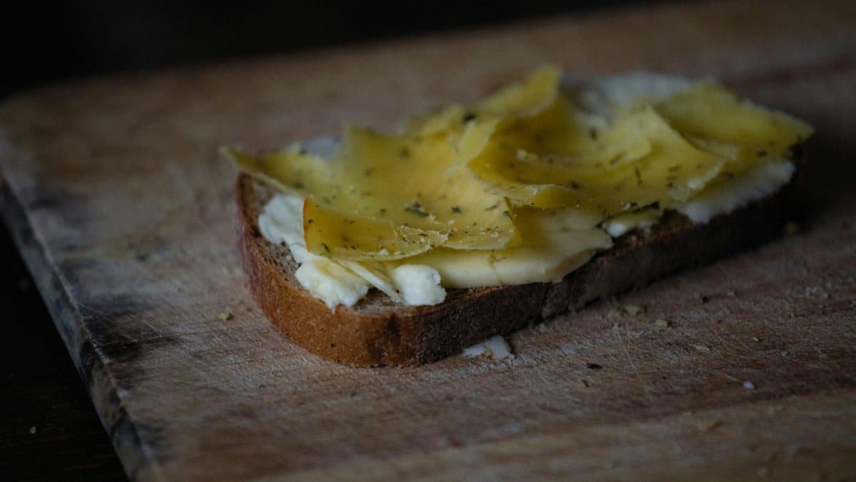 Close-up of rustic bread topped with butter and cheese slices on wooden board, perfect for breakfast or snack.