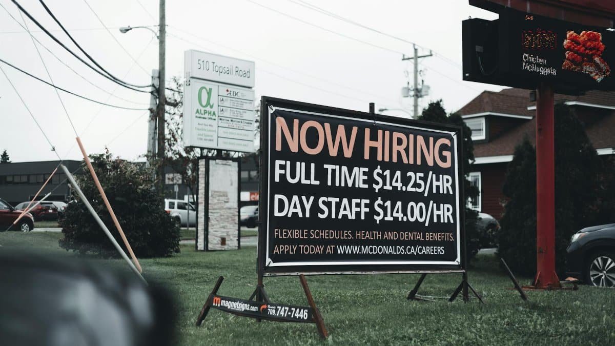 Outdoor hiring sign advertising restaurant job openings with competitive wages and benefits.