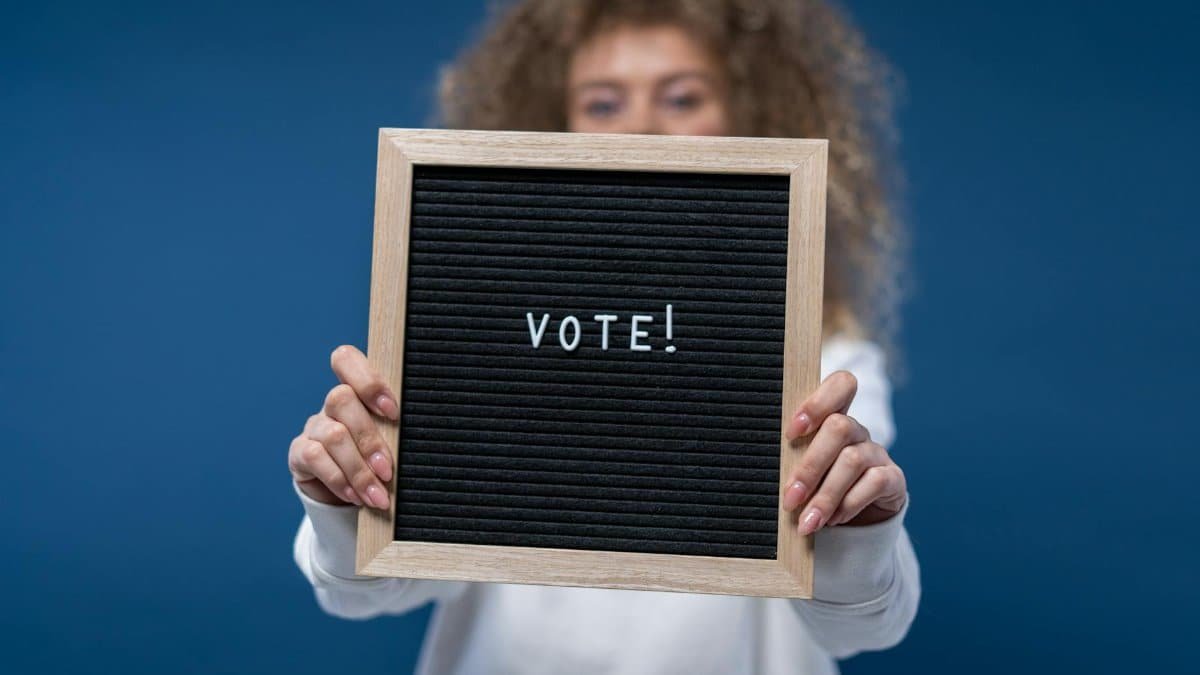 Woman holding a wooden framed board with 'Vote!' text, highlighting democratic participation.