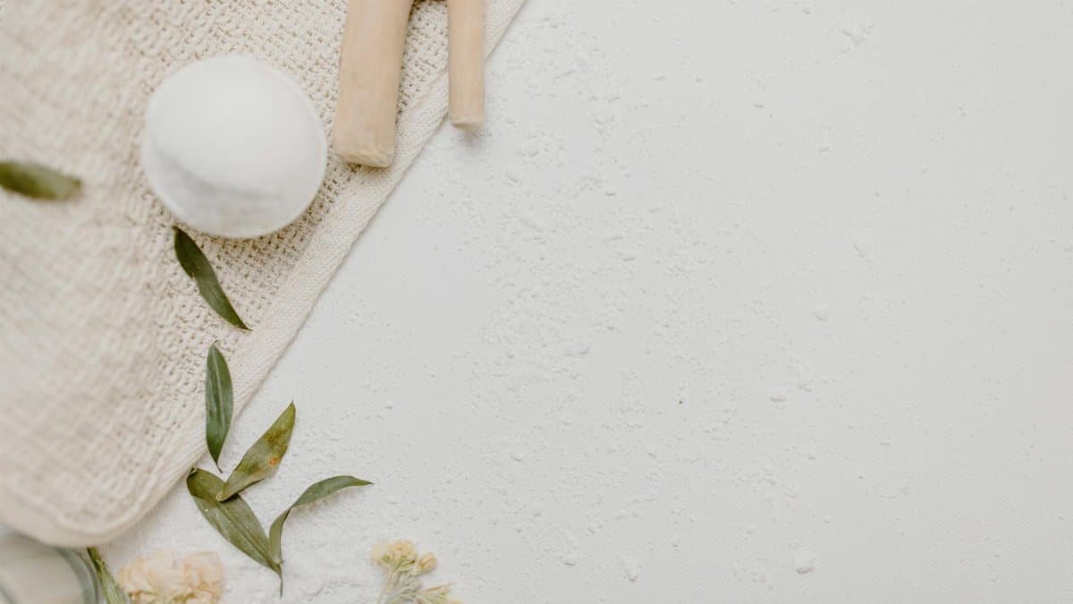 Top view of a spa bath set with a bath bomb, leaves, and flowers on a textured background.