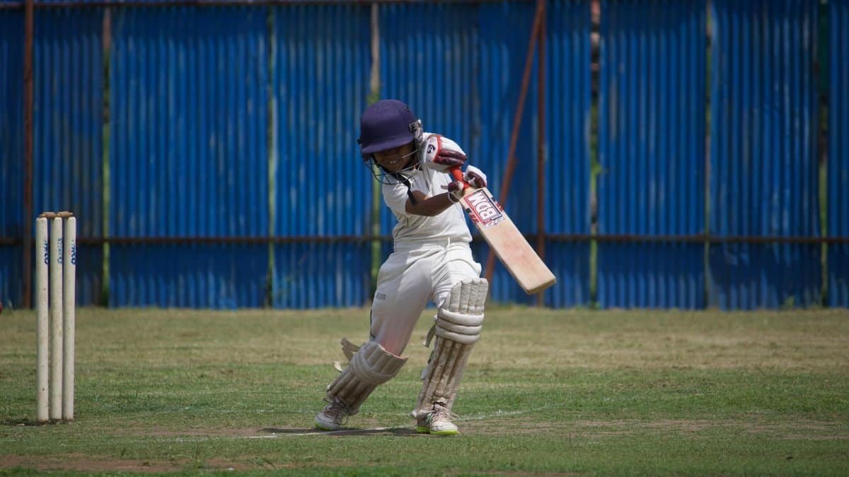 A young cricketer in action on a sunny day, playing on a grass field with a bat and wicket.