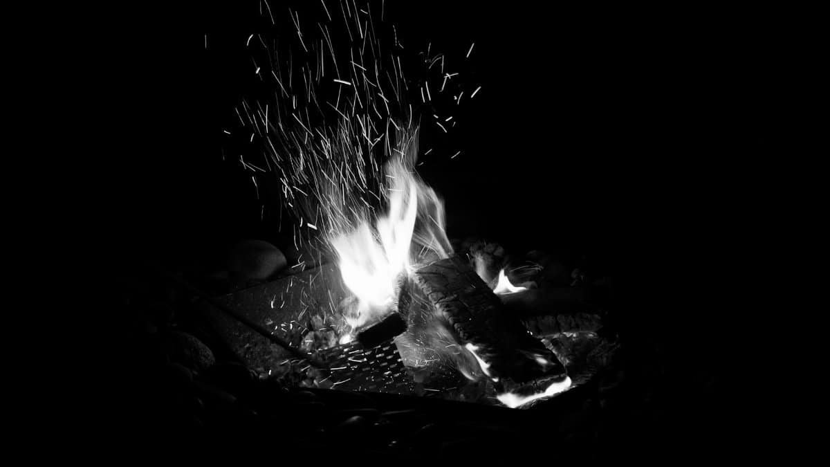 A mesmerizing black and white photo capturing a campfire's flames and sparks in a dark night setting.