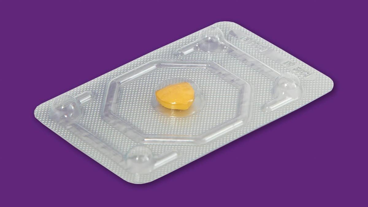 A yellow pill in a blister pack on a vibrant purple background, representing healthcare.