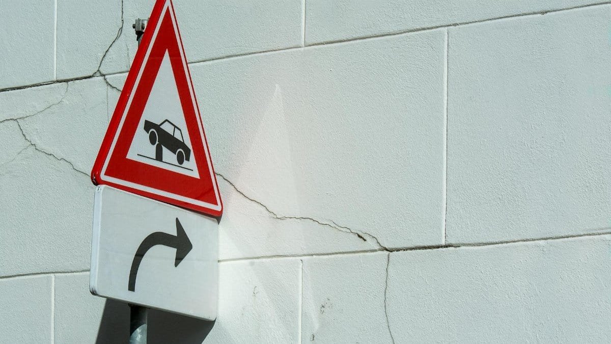 Traffic warning sign on a cracked white wall, indicating a turn ahead.