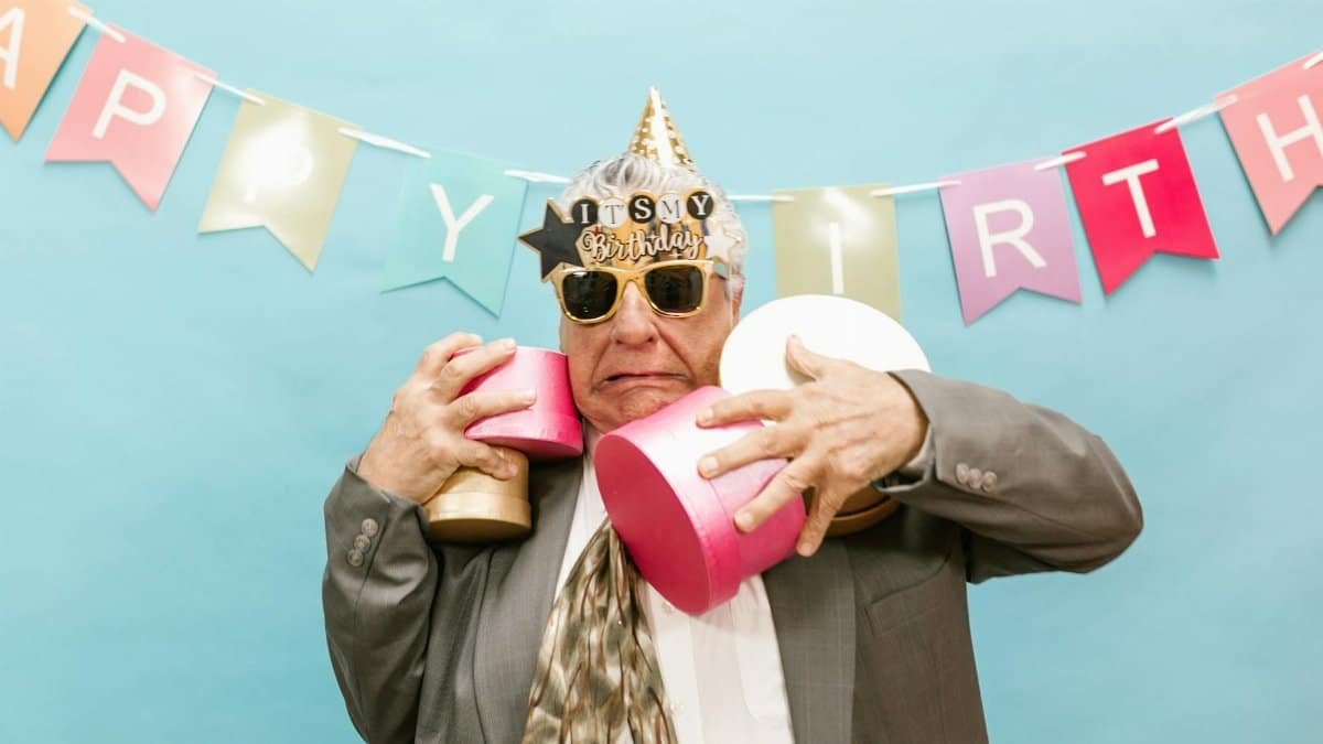Elderly man joyfully celebrating his birthday with gifts and decorations.