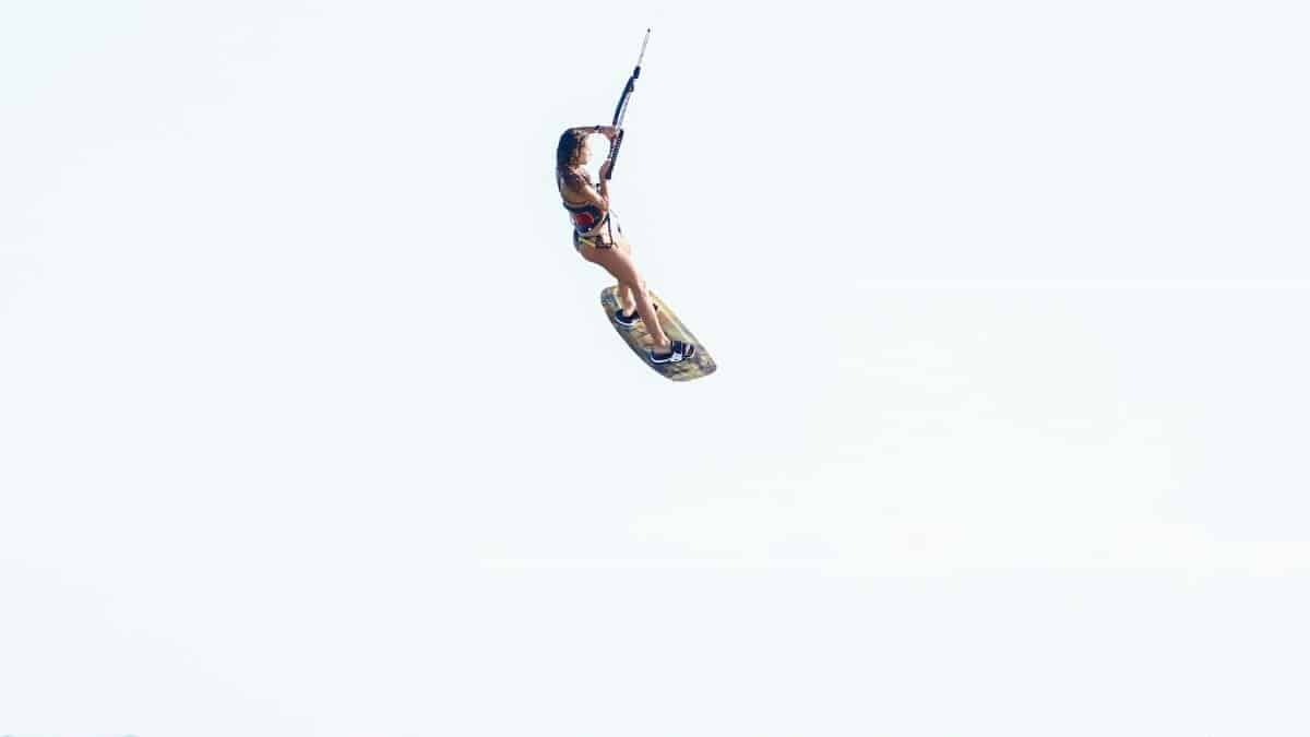 A woman skillfully kiteboarding high above ocean waves in daylight, showcasing thrilling aerial maneuvers.